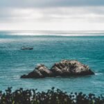 A Big rocks in the middle of the sea and a coast guard sailing in the distance